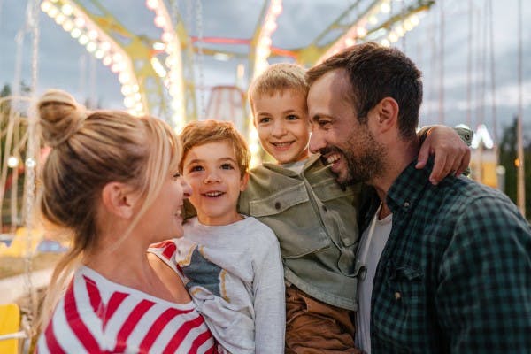 Familie med to barn smiler og ser på hverandre i en fornøyelsespark